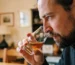 Un homme barbu hume attentivement un verre de dégustation de whisky ambré, en gros plan.