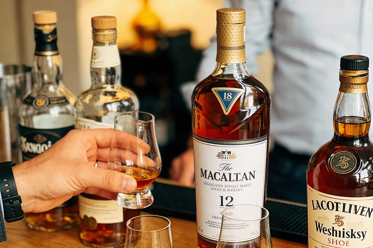 Dégustation de whisky avec bouteilles, incluant The Macallan 12, des verres et une main tenant un verre rempli.