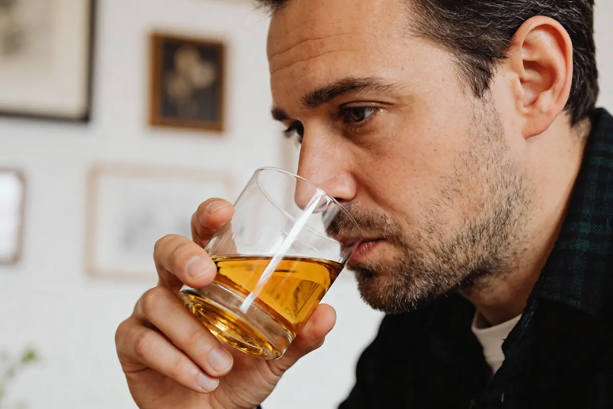 Gros plan d'un homme barbu dégustant une boisson ambrée dans un verre.